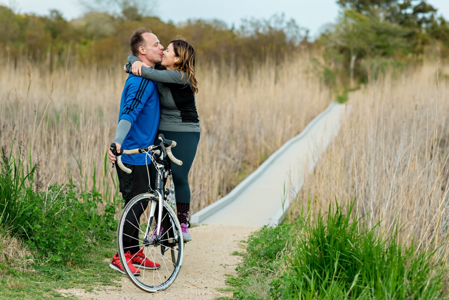 A silly couple fool around on bikes by the beach in their engagement session.